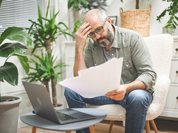 Confused man looking at papers and laptop