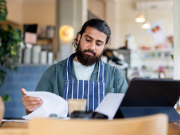 Cafe owner looking at paperwork and laptop