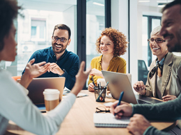 Employees sitting collaborating around an office table smiling and talking