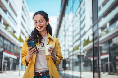 Smiling female walking, while holding coffee and phone