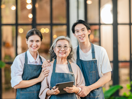 Smiling grandma and grandkids in aprons with ipad standing outside business