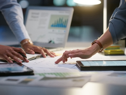 Hands working on paper charts and graphs spread out on table