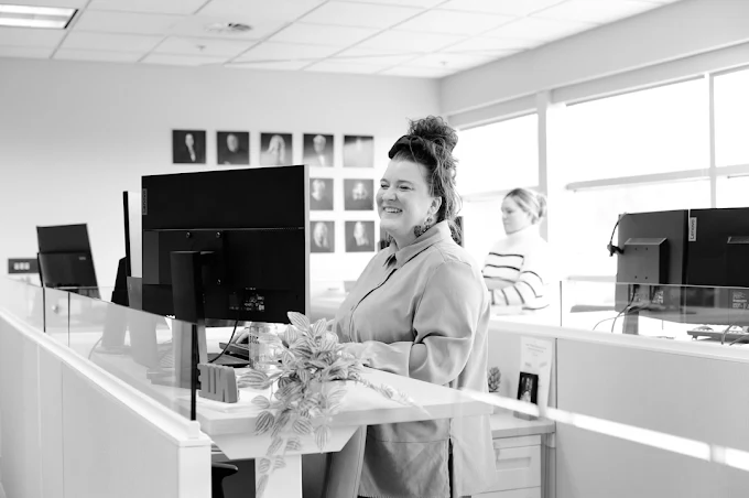 woman standing at her desk while looking at the computer and smiling.