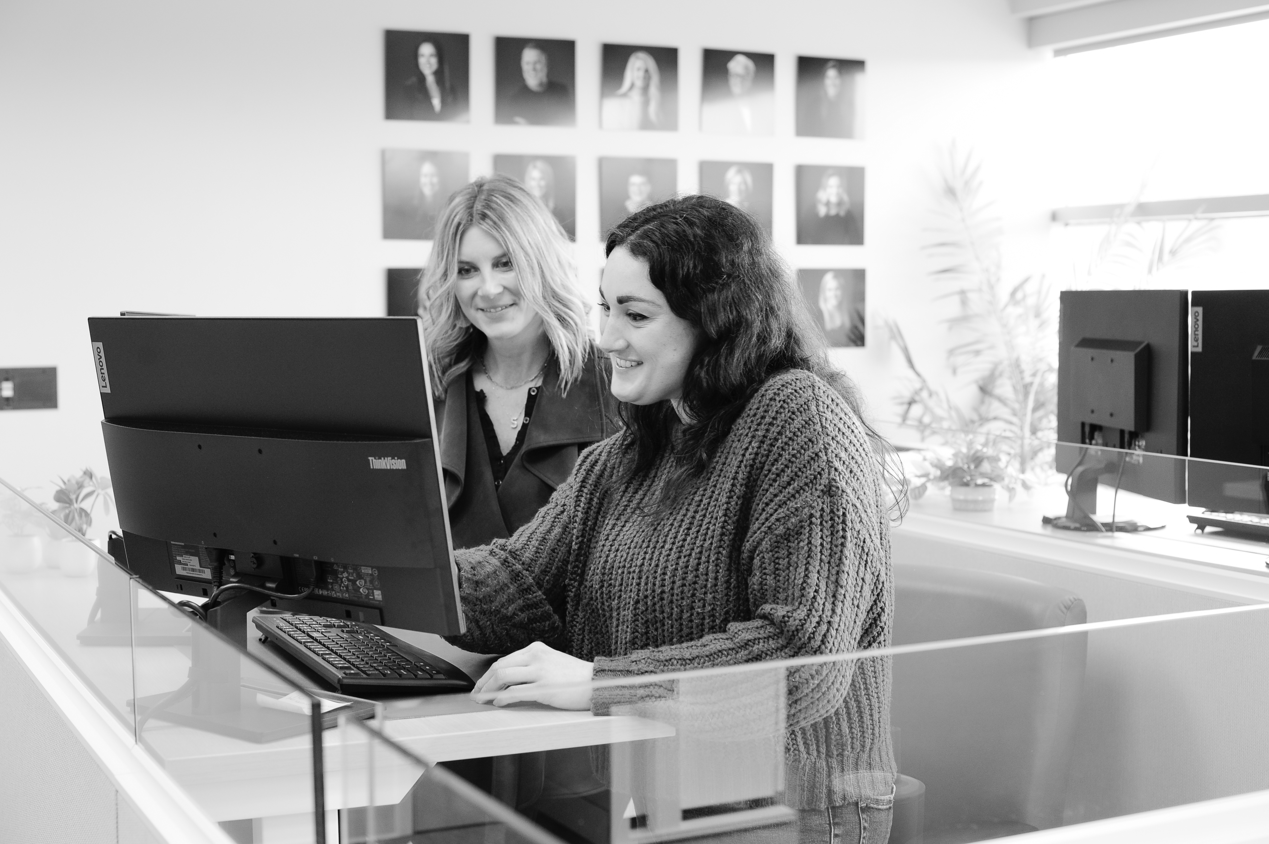 Ask About Our HR Services two women standing at a desk smiling while looking at a laptop.