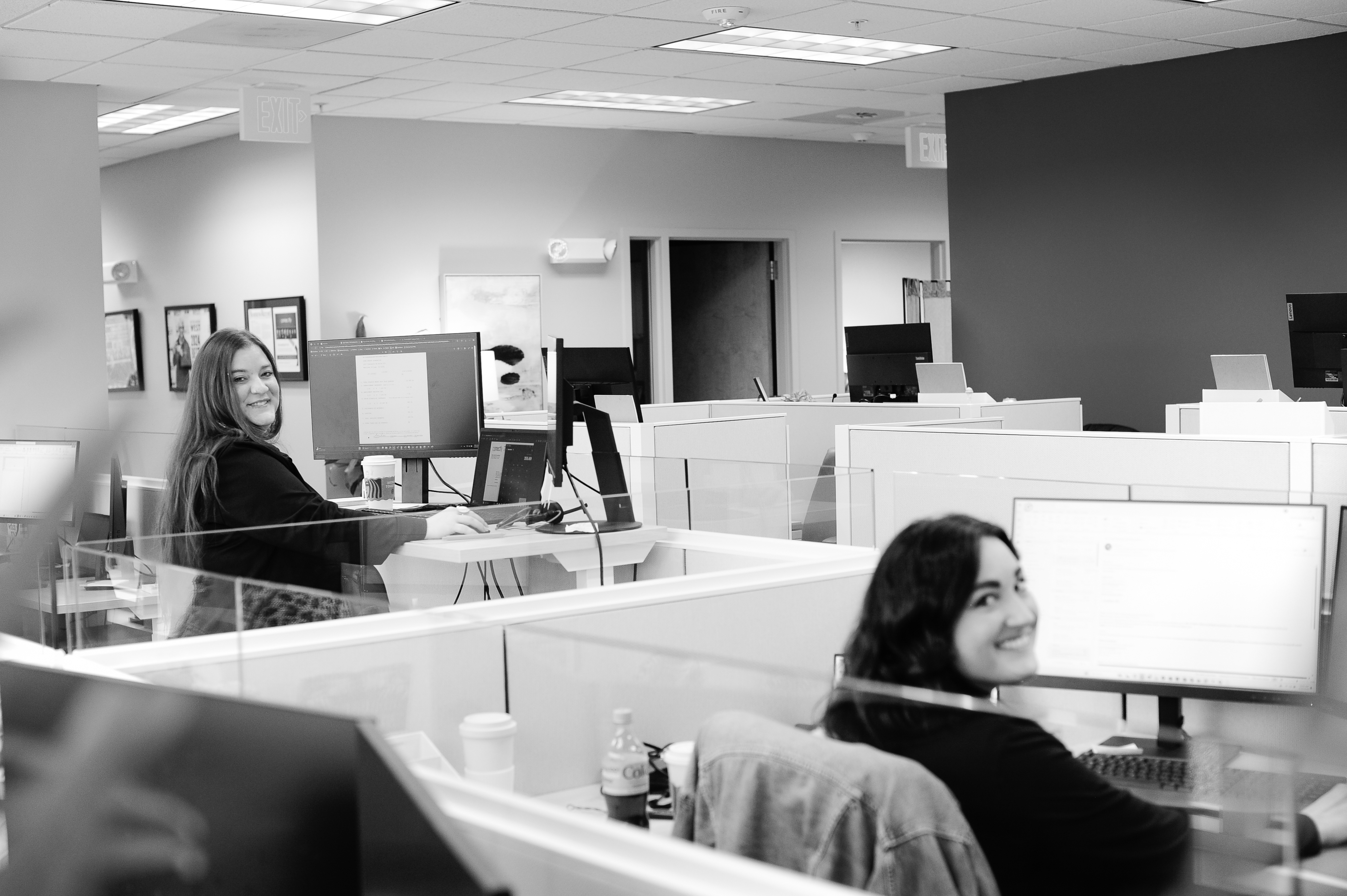 two women sitting at their desks looking back and smiling.